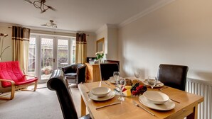 A dining area with a wooden table set for four, chairs, a red armchair, and a view of the garden through the glass door.