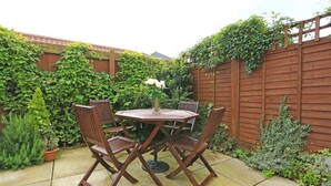 A patio with a round table and four chairs, surrounded by a wooden fence and lush greenery.