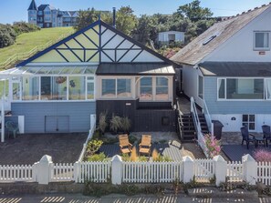 Une maison dotée d’une grande véranda en verre, d’une terrasse en bois et d’un jardin clos.