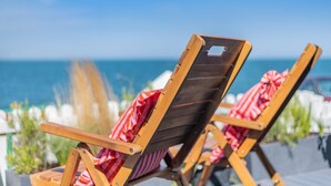 Zwei Holzliegen mit gestreiften Kissen, auf einer Terrasse mit Blick auf das Meer.