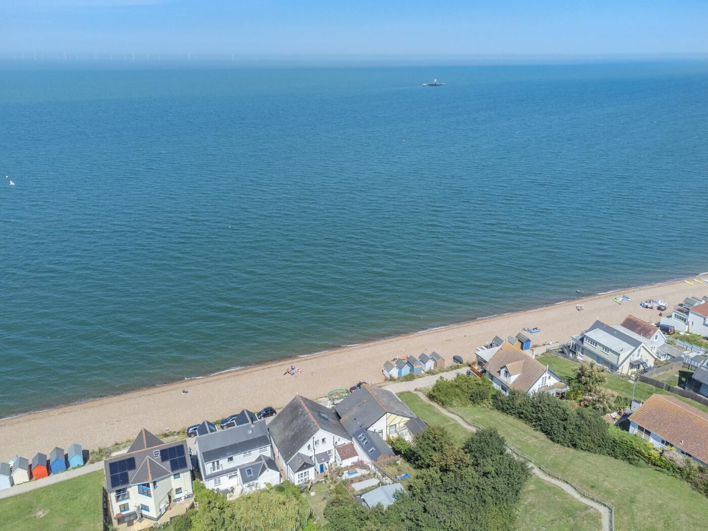 Vue aérienne d’une zone résidentielle côtière, avec des maisons, une plage et un bateau au loin.