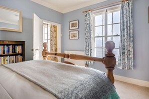 A bedroom with a bed, a wooden headboard, a bookshelf, and a window with curtains. - 3 Bed in Southwold (oc-eas) (Southwold)