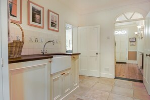 A kitchen with white cabinetry, a wooden countertop, and a tiled backsplash. There are framed pictures on the wall, a basket on the counter, and a door leading to another room. - 3 Bed in Southwold (oc-eas) (Southwold)