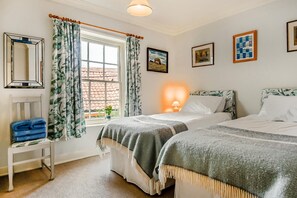 Quarto com duas camas, janela com cortinas, mesa de cabeceira com toalhas e decoração na parede.