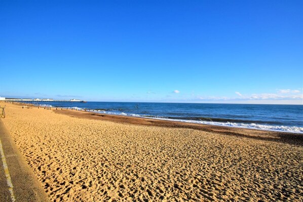 Uma extensa praia de areia com céu azul e límpido.