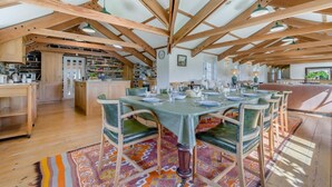Un vaste espace à manger doté d’un haut plafond en bois, d’un îlot central et offrant une vue sur la cuisine et le salon.