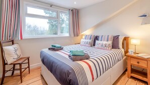 Un dormitorio con una cama grande, cortinas a rayas, una silla de madera y una mesita de noche con lámpara.