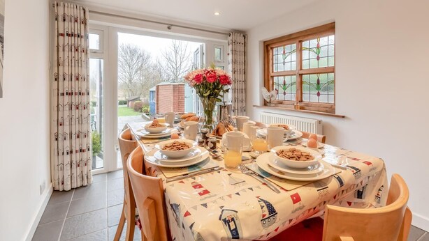 Un área de comedor con una mesa lista para el desayuno, un florero con flores y una ventana con vistas al exterior.