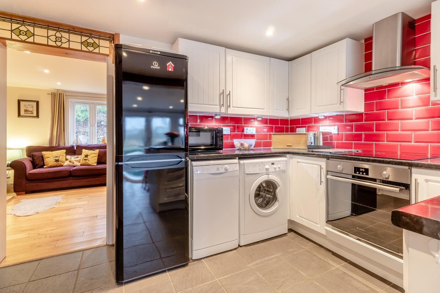 A modern kitchen with white cabinets, a red backsplash, a black refrigerator, a washing machine, and an oven.