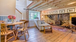 A cozy living room with a stone fireplace, wooden beams, a dining area with a table set for four, and a comfortable sofa. - 1 Bed in Tresillian (oc-t32988) (Tresillian)