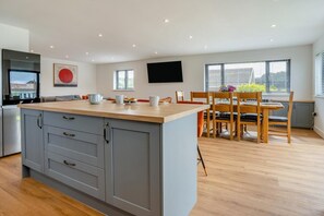 A modern kitchen with grey cabinets, a wooden countertop, and a dining area with a table and chairs. - 4 Bed in Brecon (oc-m32973) (Brecon)