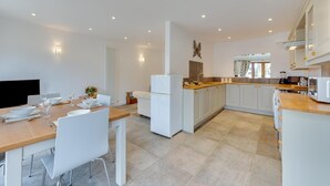 Eine moderne Küche mit weißen Schränken, einer zentralen Kochinsel und einem Essbereich mit einem Holztisch und weißen Stühlen.