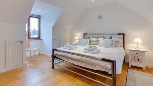 Ein modernes Schlafzimmer mit schrägen Wänden, einem Bett mit ordentlich gefalteten Handtüchern, einem Sessel und einem Nachttisch mit Lampe.