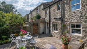 A stone building with a patio area featuring a table and chairs, surrounded by potted plants and flowers. - 3 Bed in Hardraw (oc-ds1029) (Appersett)