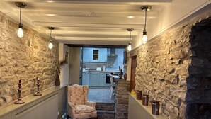 A hallway with stone walls, a chair, a rug, and a kitchen in the background. - 3 Bed in Hardraw (oc-ds1029) (Appersett)