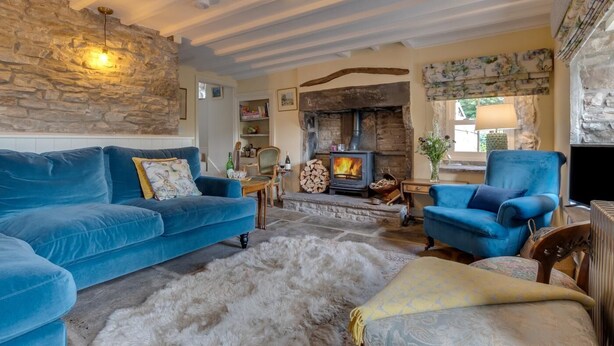 A cozy living room with a stone wall, a fireplace, a blue sofa, and a blue armchair. - 3 Bed in Hardraw (oc-ds1029) (Appersett)
