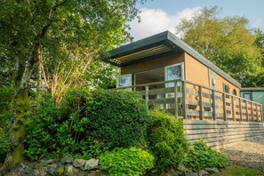 A modern house with a large glass window, surrounded by lush greenery and a wooden fence. - 1 Bed in Newby Bridge (oc-b32969) (Newby Bridge)
