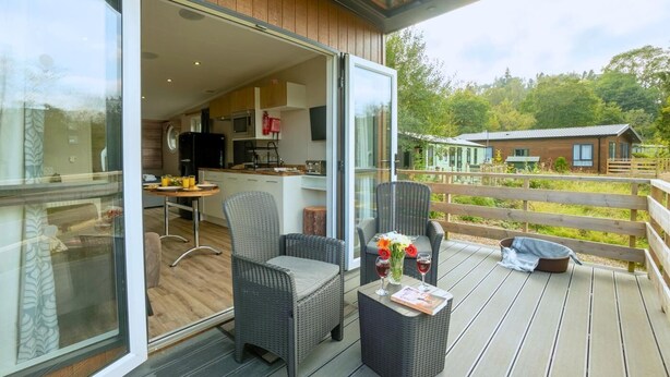 Ein moderner Essbereich im Freien mit Korbmöbeln, einem Tisch mit Getränken und Blick auf eine Holzterrasse und viel Grün.