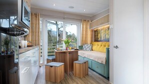 Ein kleines Zimmer mit einem Bett, einem Tisch mit Hocker, einer Küchenzeile und Blick durch eine Glastür.