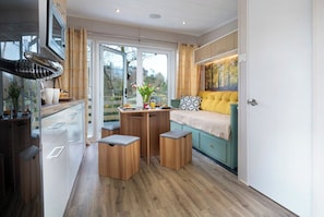 A compact room with a bed, a small table with stools, a kitchenette, and a view through a glass door.