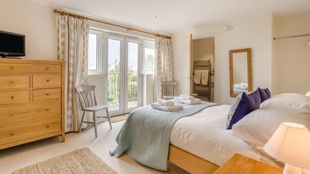 Une chambre à coucher comprenant un lit, une télévision, une commode en bois, une chaise et un balcon avec des rideaux.