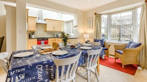 Un coin repas avec une table dressée pour quatre personnes, une cuisine en arrière-plan et une vue sur un balcon.
