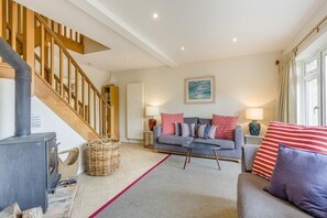 Ein Wohnzimmer mit Sofa, Tisch, Kamin, Treppe und Fenster.