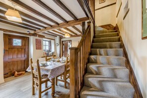 Un escalier en bois avec des marches recouvertes de moquette, un coin repas avec une table dressée pour quatre personnes, et une porte en bois avec une fenêtre.