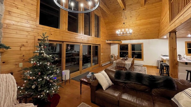 Een gezellig chaletinterieur met houten details, een kerstboom, een leren bank en een eethoek met een tafel en stoelen.