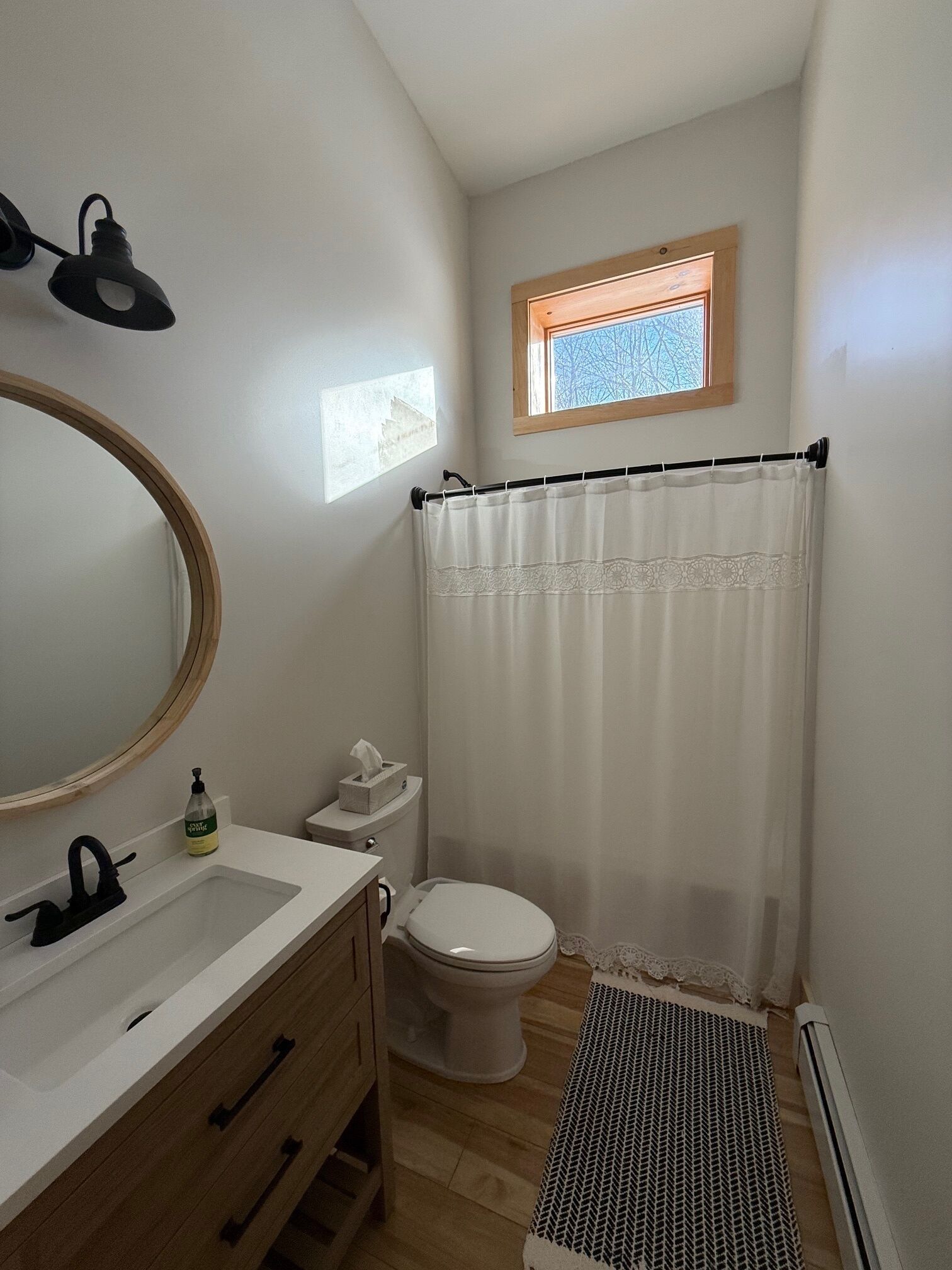 A bathroom with a wooden vanity, a round mirror, a toilet, and a shower curtain.