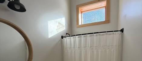 A bathroom with a wooden vanity, a round mirror, a toilet, and a shower curtain.