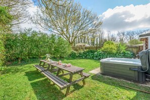 Un jardin avec une table de pique-nique en bois, un jacuzzi et une végétation luxuriante.