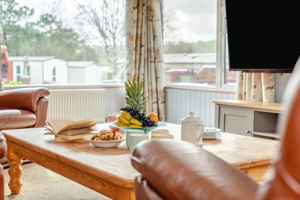 A cozy living room with a wooden coffee table, a book, a fruit bowl, and a television.