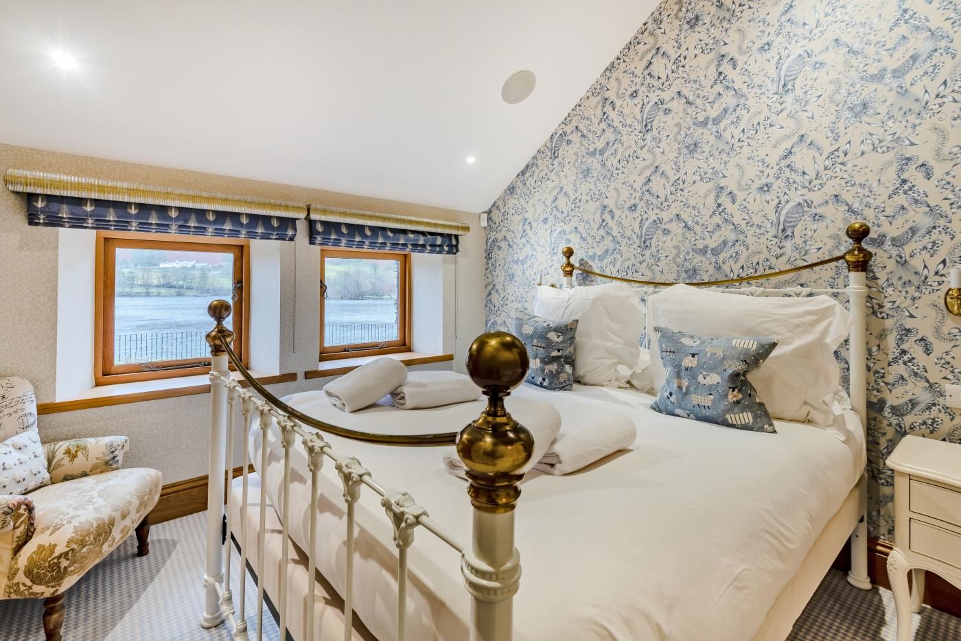 A bedroom with a bed, two windows, a chair, and a nightstand.