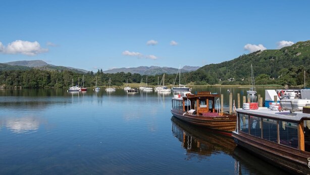 Ein ruhiger See mit mehreren angestaubten Booten, umgeben von grünen Hügeln und blauem Himmel.