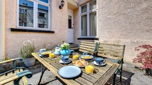 Ein Essbereich im Freien mit einem Holztisch, gedeckt für ein Frühstück, umgeben von Topfpflanzen und einer Bank.