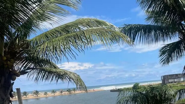 A round table with orange chairs and a white tablecloth, set against a backdrop of a beach and palm trees. - Lagoona Ocean Suites Monrovia Thinker’s Village (Mills Center)