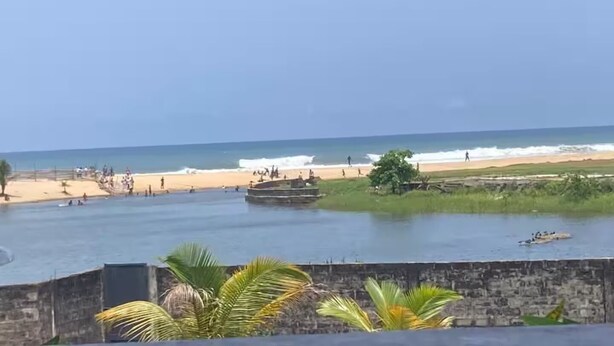 Une plage avec une mer calme, quelques bateaux et des gens qui profitent du bord de mer.