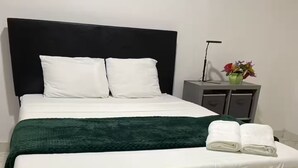 A neatly made bed with white linens, a dark headboard, and a green throw blanket. - Lagoona Ocean Suites Monrovia Thinker’s Village (Mills Center)
