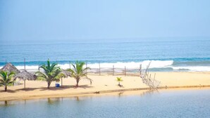 A beach with palm trees, a thatched-roof hut, and a wooden fence. - Lagoona Ocean Suites Monrovia Thinker’s Village (Mills Center)