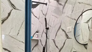 Une salle de bain avec des murs en marbre, un lavabo en forme de bol de couleur verte, une douchette à main et des bacs de rangement.