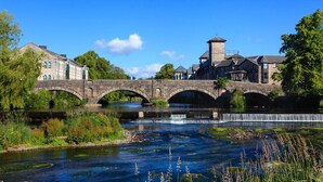 A stone bridge over a river with a waterfall, surrounded by greenery and historic buildings. - 2 Bed in Kendal (oc-gl097) (Kendal)
