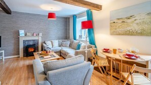 A cozy living room with a fireplace, a sofa, a dining table with chairs, and a painting on the wall. - 2 Bed in Kendal (oc-gl097) (Kendal)