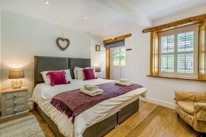 Ein Schlafzimmer mit einem großen Bett, einem Nachttisch, einem Sessel, einem Fenster mit Jalousien und einer herzförmigen Dekoration an der Wand.
