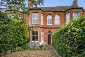 A two-story brick house with a front entrance, a small porch, and a garden area with plants and a gravel path. - 3 Bed in Southwold (oc-rvil) (Southwold)