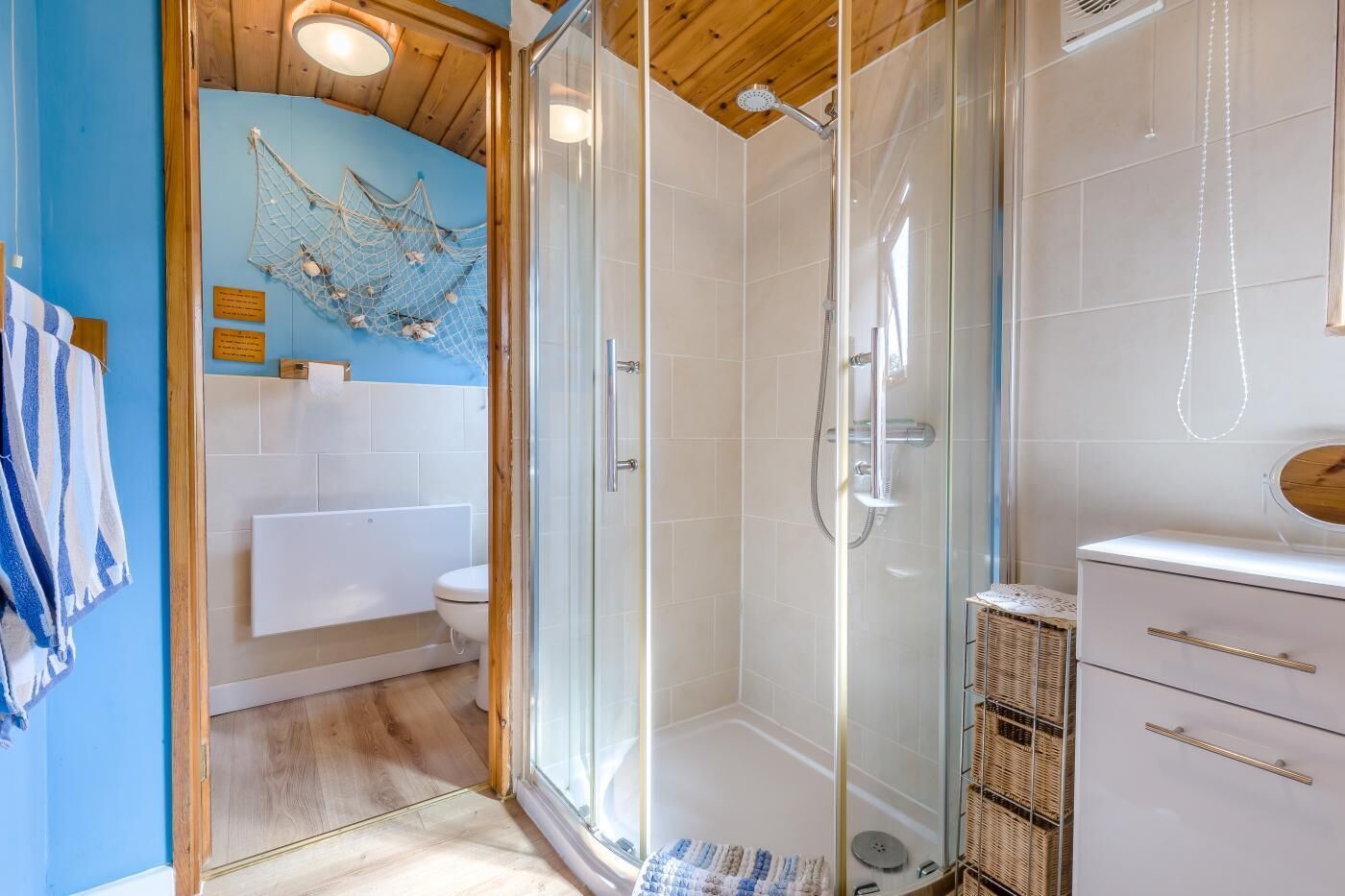 Een moderne badkamer met een douchecabine van glas, een witte wastafel en een blauwe muur met een netdecoratie.