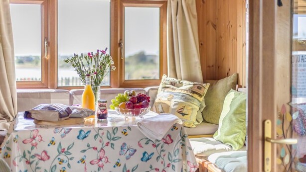 A cozy cabin interior with a wooden interior, a table with a floral tablecloth, a bowl of fruit, and a vase with flowers. - 2 Bed in Snettisham (oc-e32982) (Snettisham)