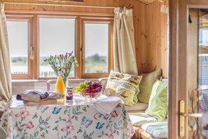 Interior acogedor de una cabaña, con paredes de madera, una mesa con mantel floral, un frutero y un jarrón con flores.