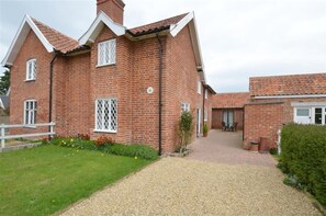 A two-story brick house with a gravel driveway, a white fence, and a garden with flowers.