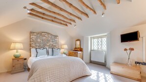 Een slaapkamer met een groot bed, houten balken in het plafond, een raam met uitzicht en een aan de muur bevestigde televisie.